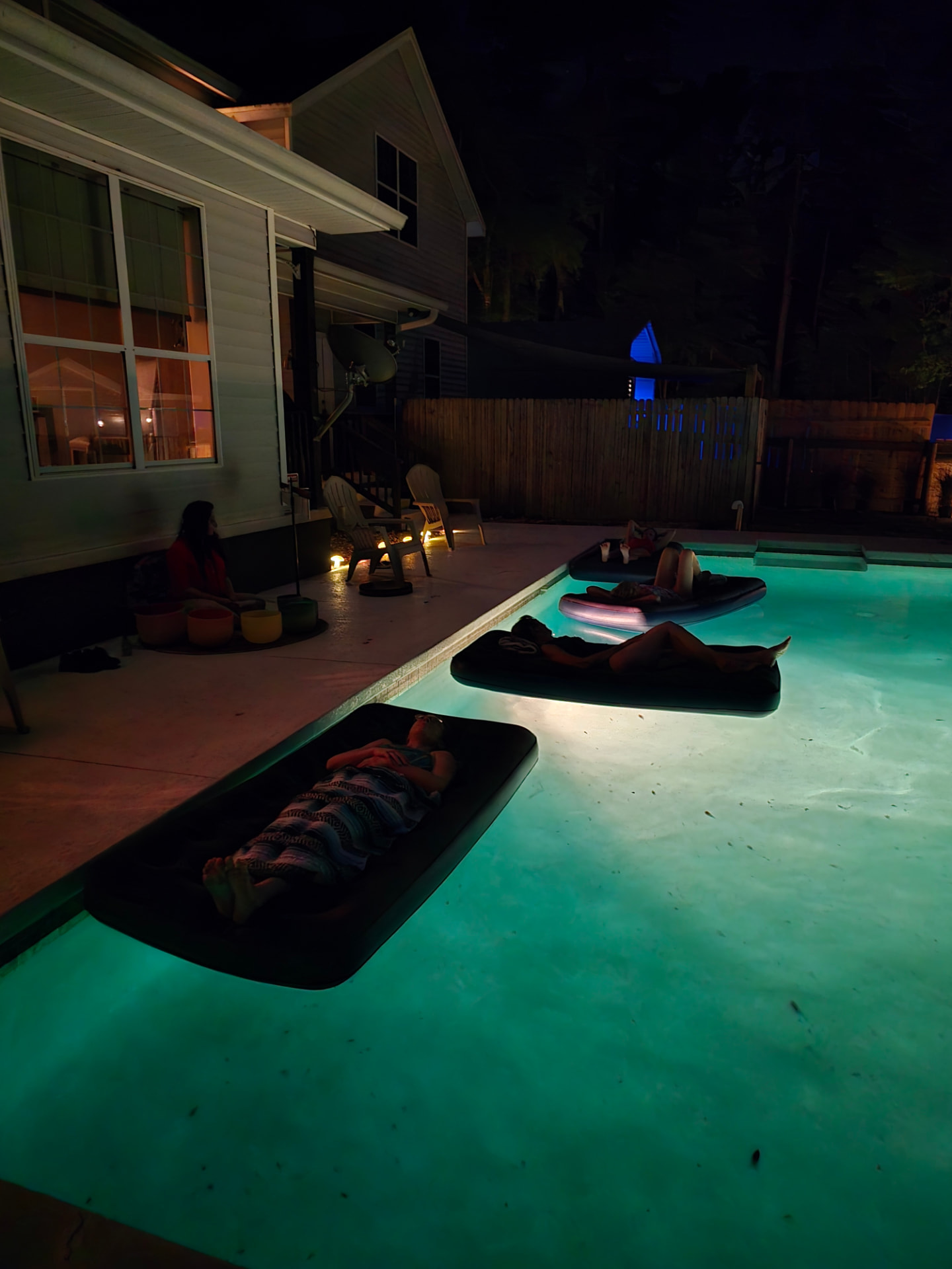 Guests resting on floats during the evening sound bath at Full Circle Retreats, with Dr. Sally Nazari playing crystal singing bowls at the pool's edge